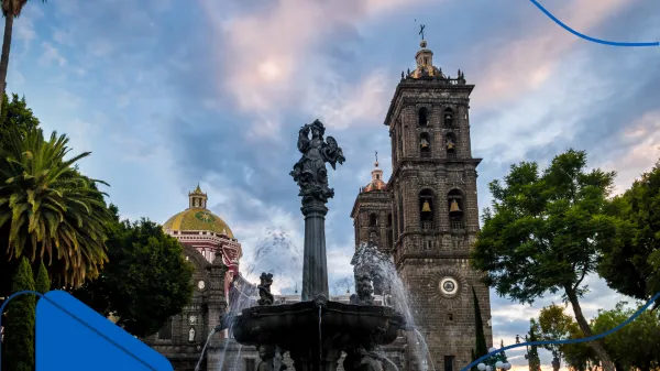 Fotografía panorámica en un atardecer de una fuente y catedral en Puebla: Una de las ciudades para comprar casa en México